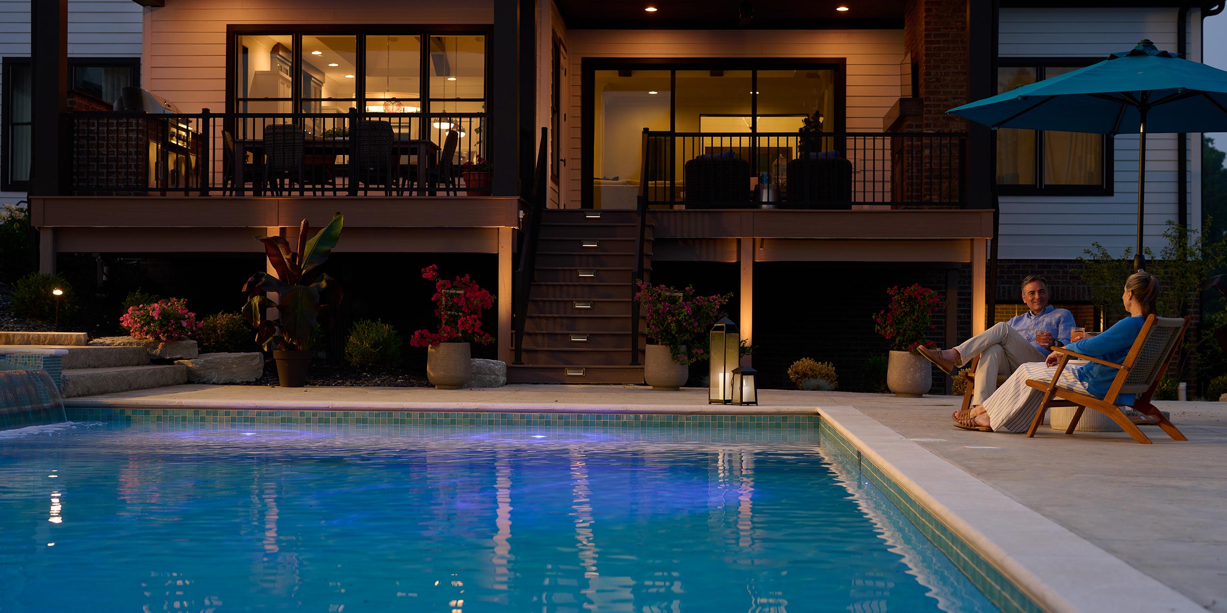 Couple sitting by a backyard pool in the evening with warm outdoor lighting