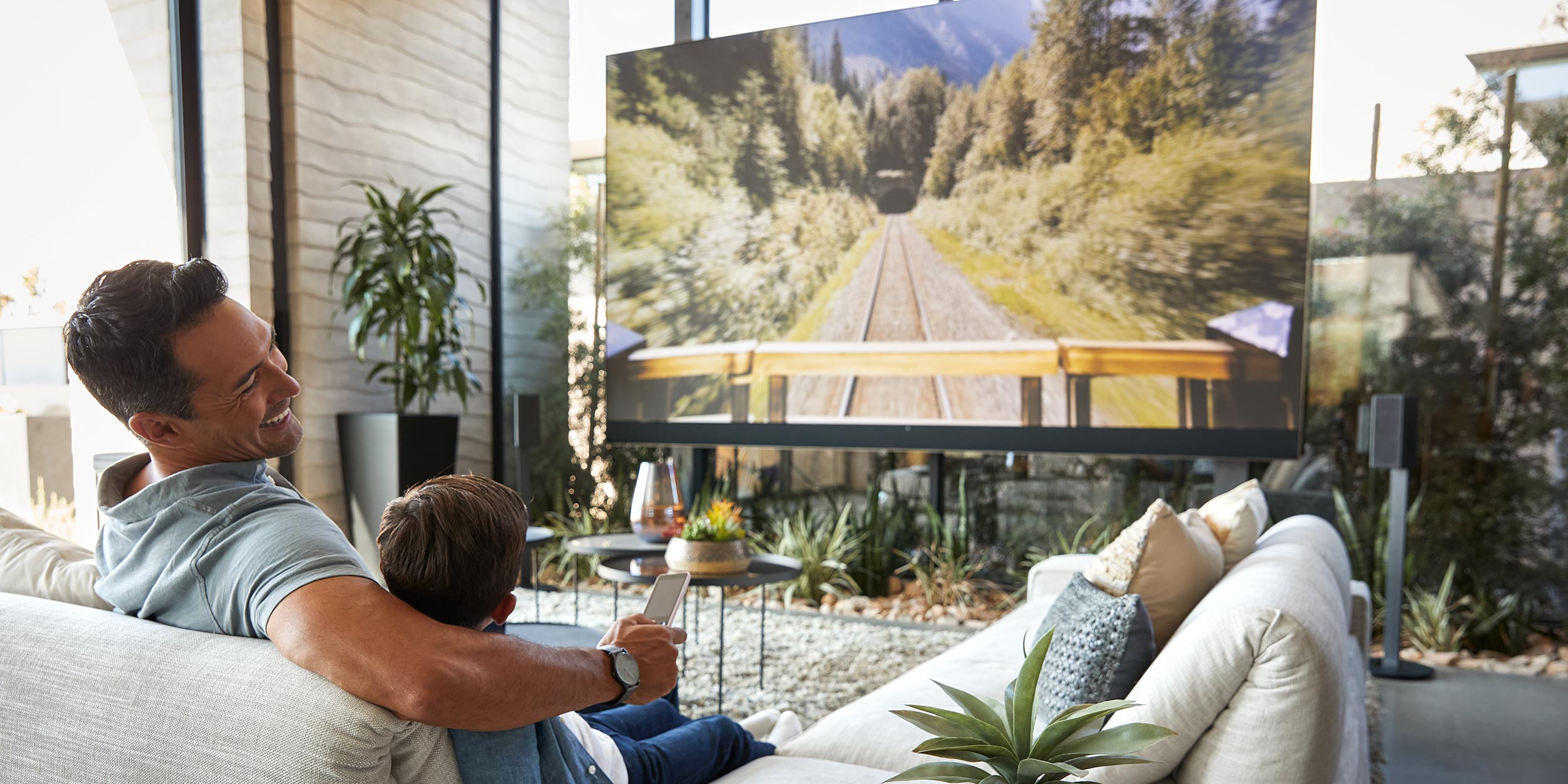 Father and son watching a large TV screen together in a modern living room